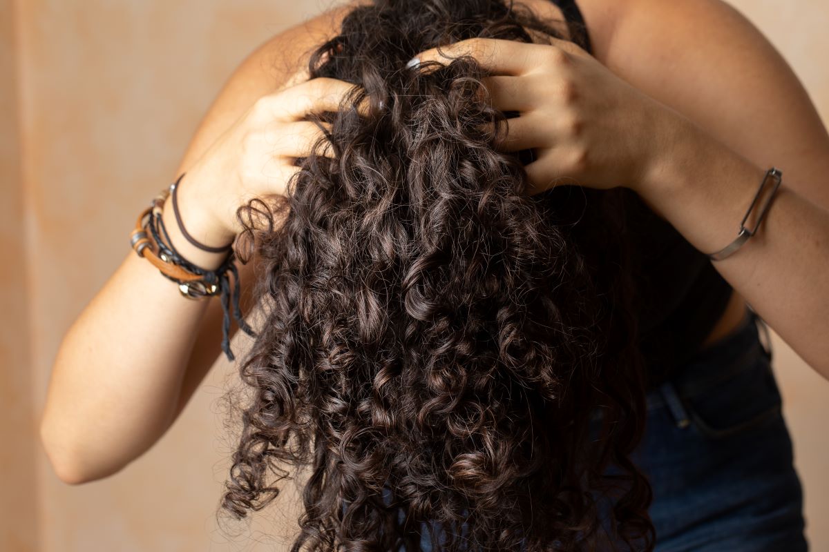 Young woman with long curly hair giving herself a scalp massage as part of her haircare routine